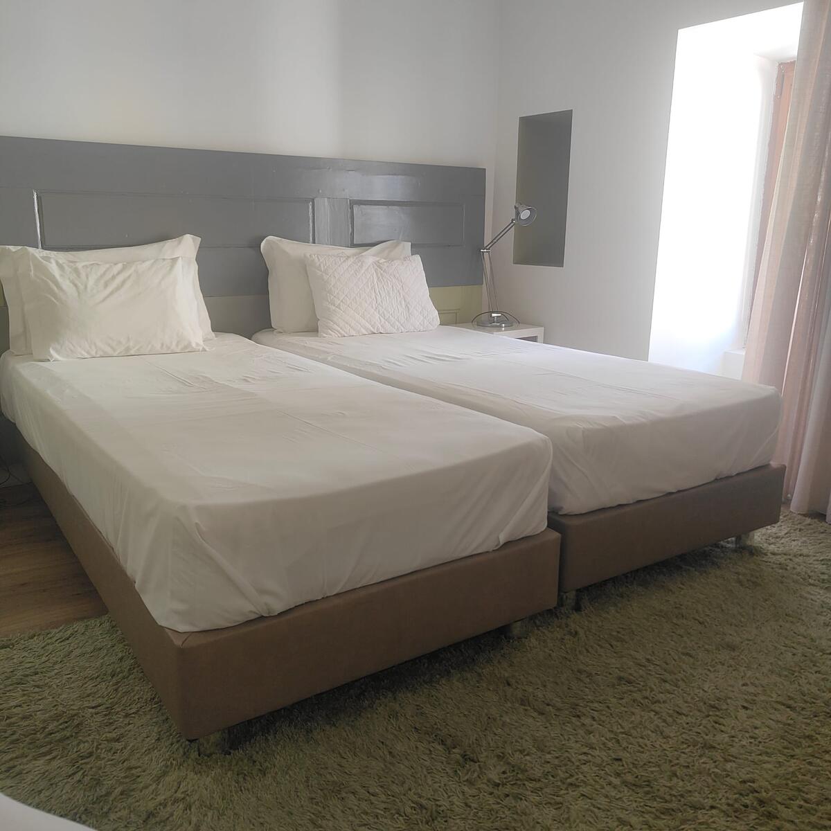 Quarto com duas camas arrumadas e roupa de cama branca